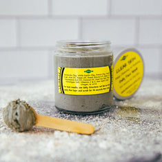Jar of gray scrub with yellow label on a textured surface